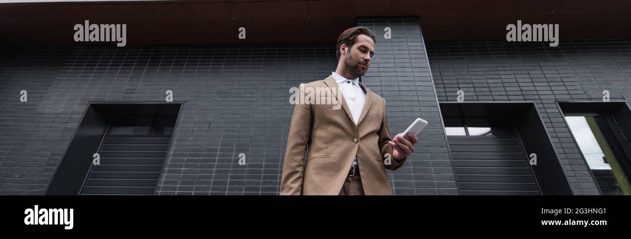 Low-Angle-Ansicht des jungen Geschäftsmannes in formeller Kleidung mit Smartphone außen, Banner Stockfoto