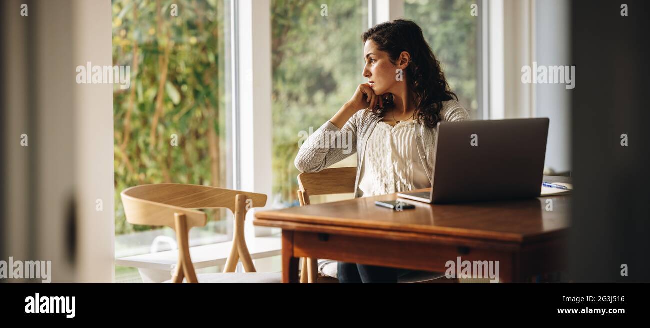 Frau, die am Tisch saß und den Laptop wegschaute. Frau, die zu Hause eine Pause von der Arbeit einnahm. Stockfoto