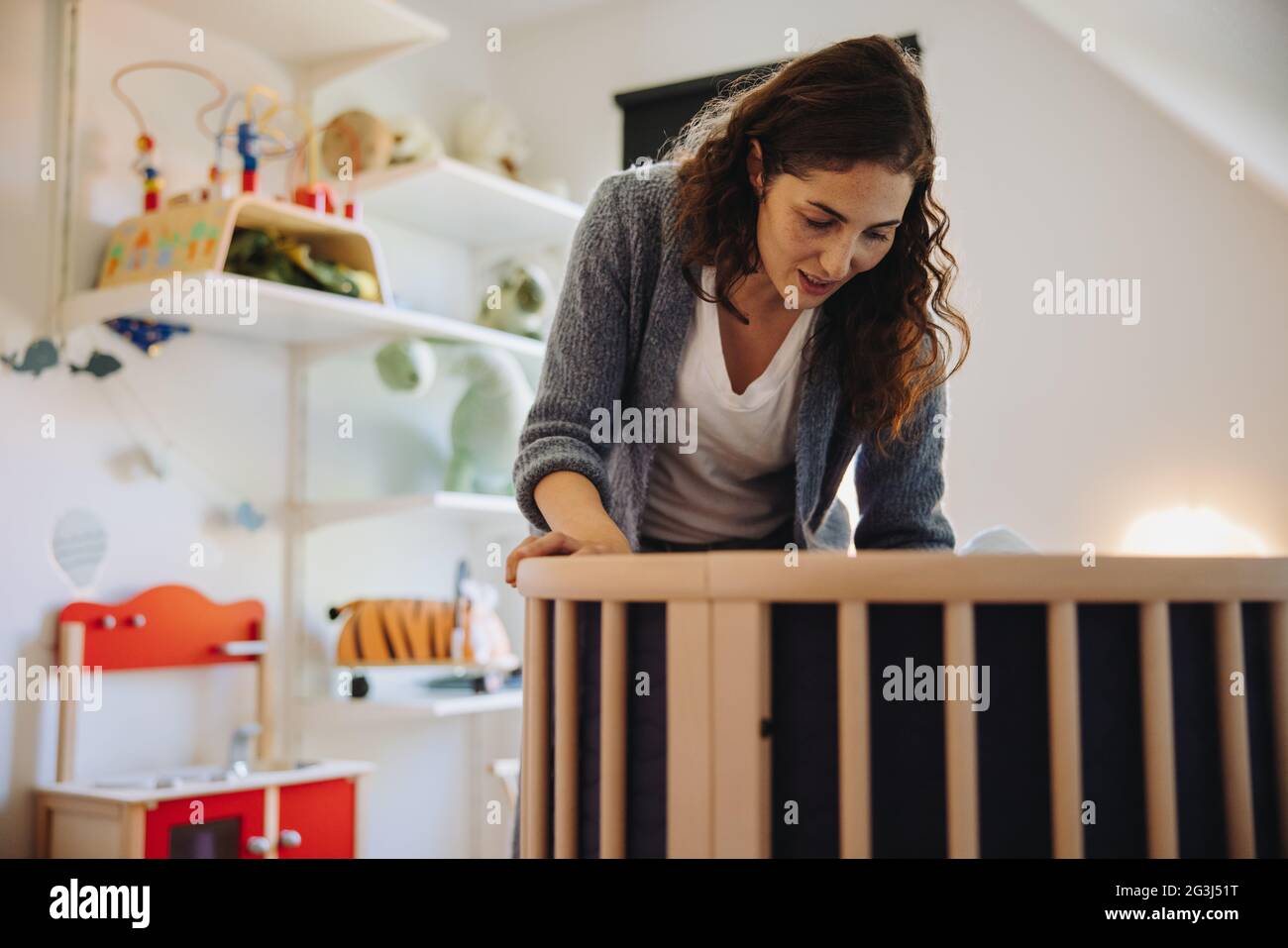 Frau, die ihr Baby in die Krippe legt. Fürsorgliche Mutter, die vor der Krippe steht und ihr Baby anschaut. Stockfoto