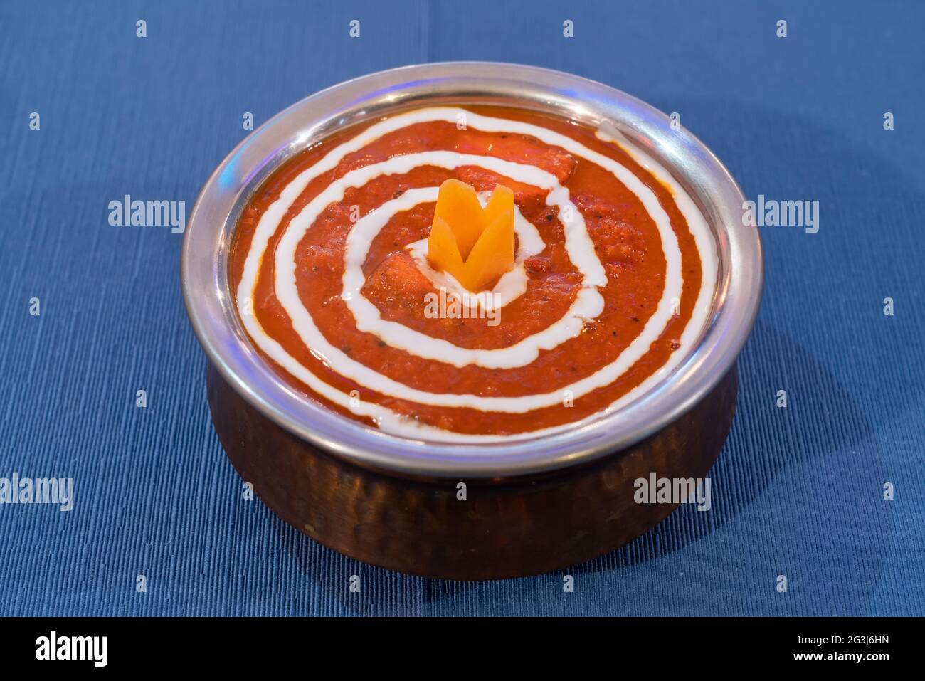 Indische Chiken Tikka Masala-Suppe. Aromatische Cremetomate auf einem Metallteller auf blauem Hintergrund. Stockfoto