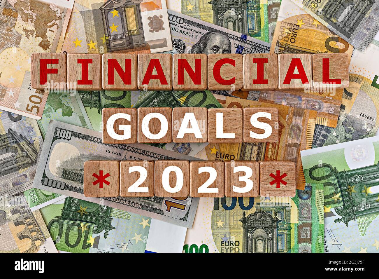 topview Foto zum Thema finanzielle Ziele. Holzwürfel mit der Aufschrift 'finanzielle Ziele 2023', auf dem Hintergrund von Dollar- und Euro-Scheinen. motiva Stockfoto
