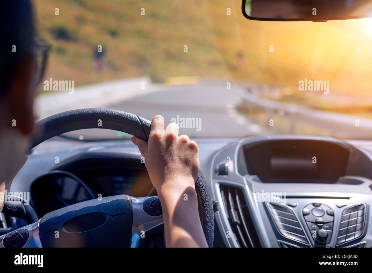 Mädchen Hände auf das Lenkrad eines Autos während der Fahrt. Vor dem Hintergrund der Windschutzscheibe und der Straße. Konzentriere dich auf ihre Hand Stockfoto