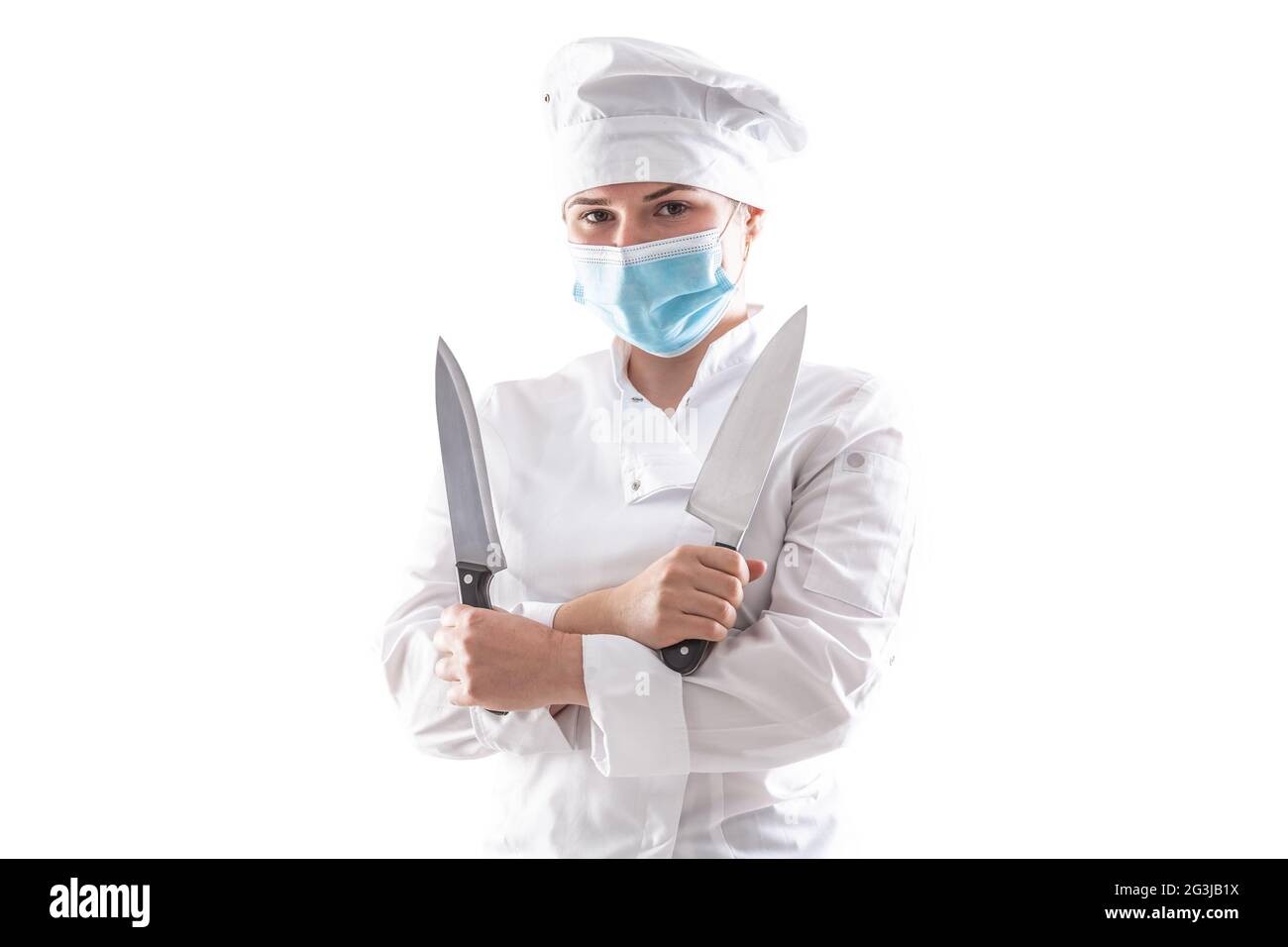Isolierter Koch mit Maske aufgrund einer Pandemie, der in einem weißen Kochmantel mit gekreuzten Händen und zwei scharfen Messern steht. Stockfoto