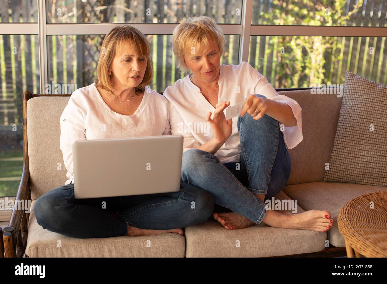 Zwei 55-jährige Frauen in legerer Kleidung verwenden einen Laptop für Videoanruf Stockfoto