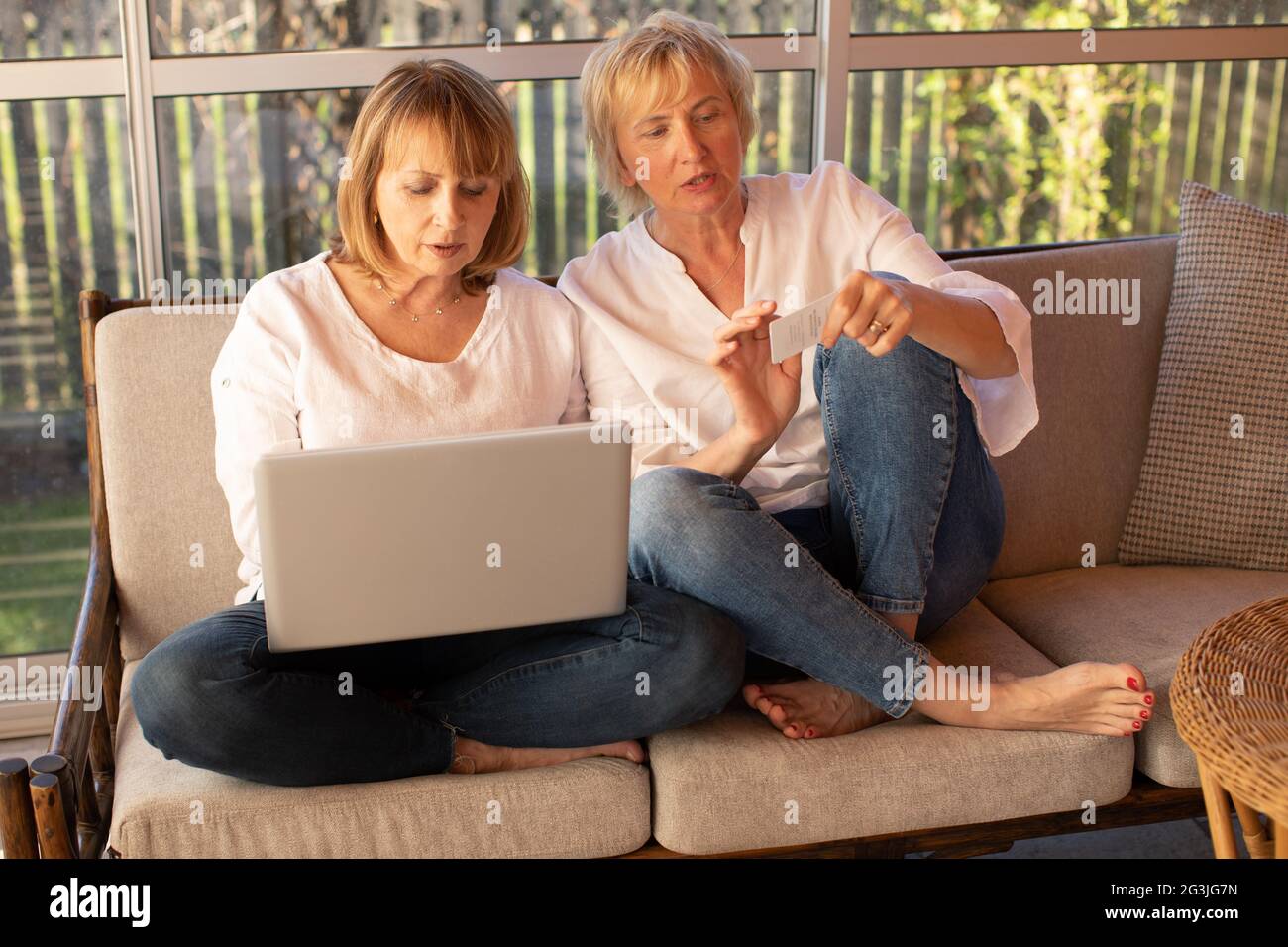 Zwei 55-jährige Frauen in legerer Kleidung verwenden einen Laptop zum Online-Shopping Stockfoto
