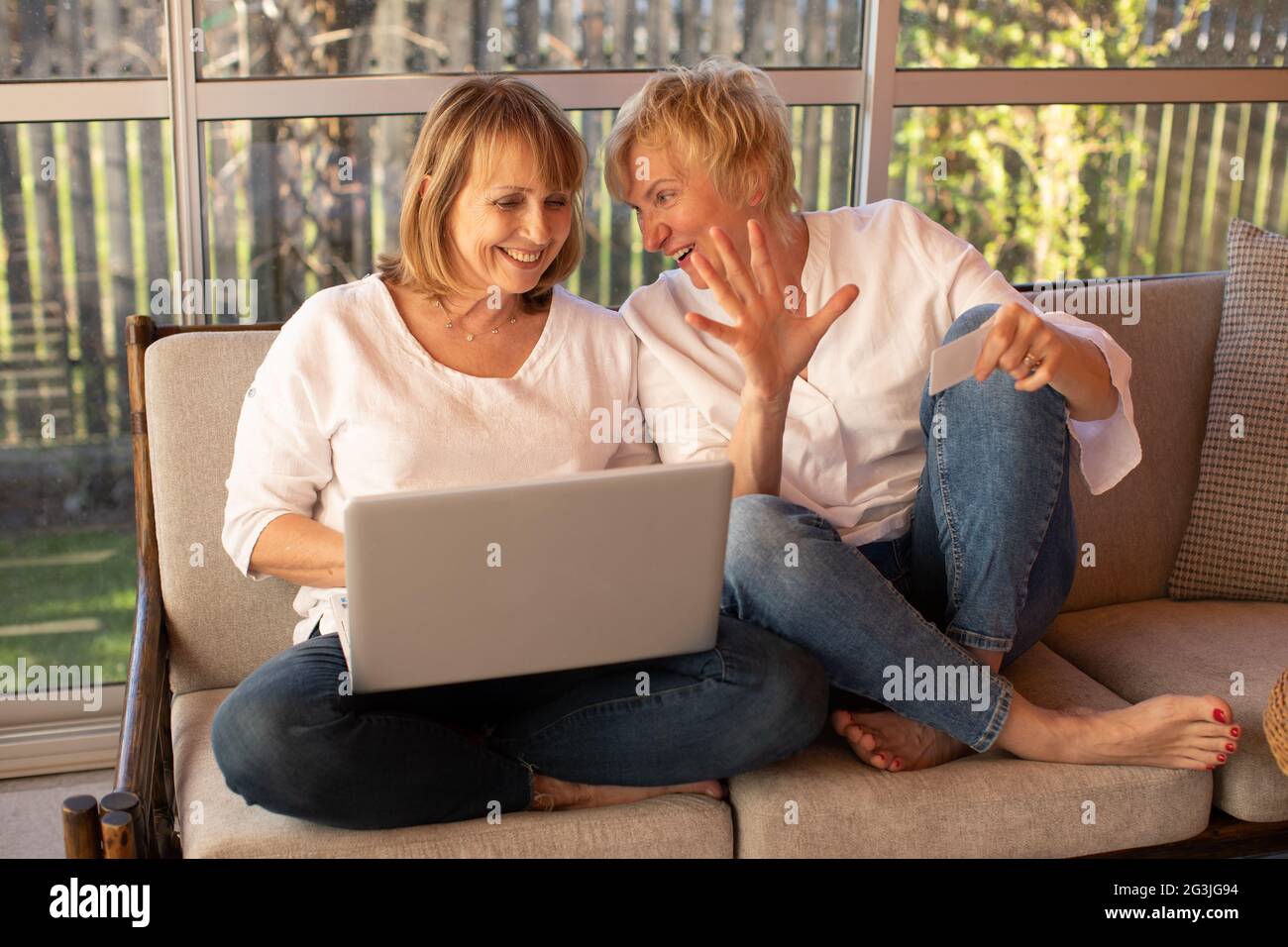 Zwei 55-jährige Frauen in legerer Kleidung verwenden einen Laptop, um zu Hause online einzukaufen Stockfoto