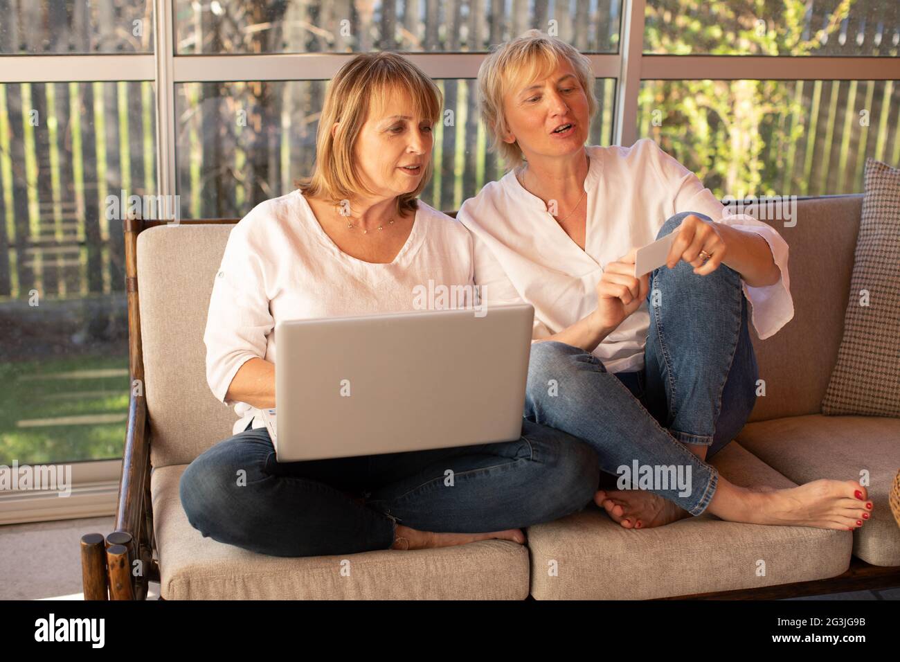 Zwei 55-jährige Frauen in legerer Kleidung kaufen online mit einem Laptop ein Stockfoto