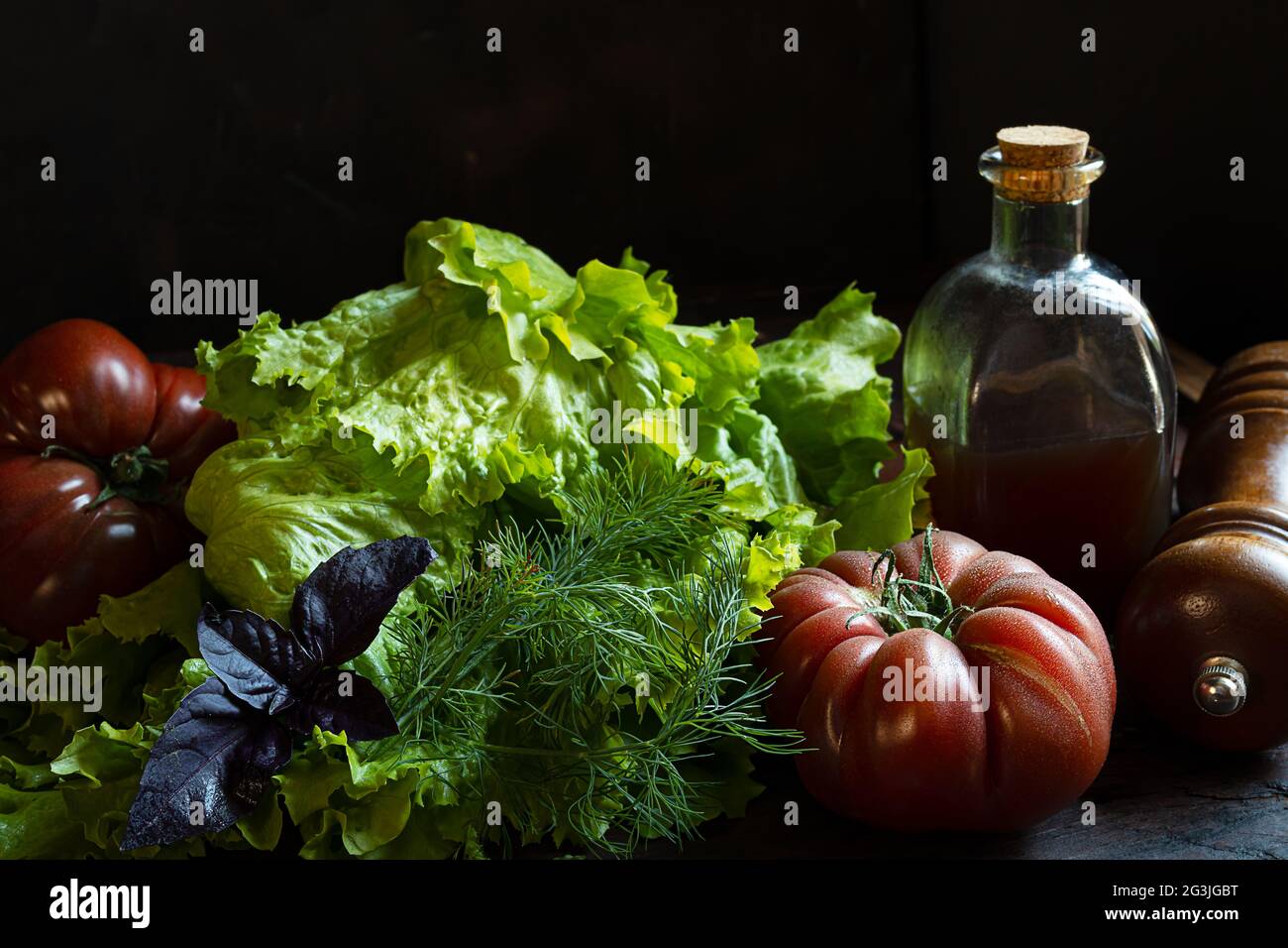 Bio-Tomaten, frischer Salat und eine Flasche mit Pumkinöl auf einem alten Holztisch, das Konzept des Gärtnerns und des Anbaus eigener Lebensmittel Stockfoto