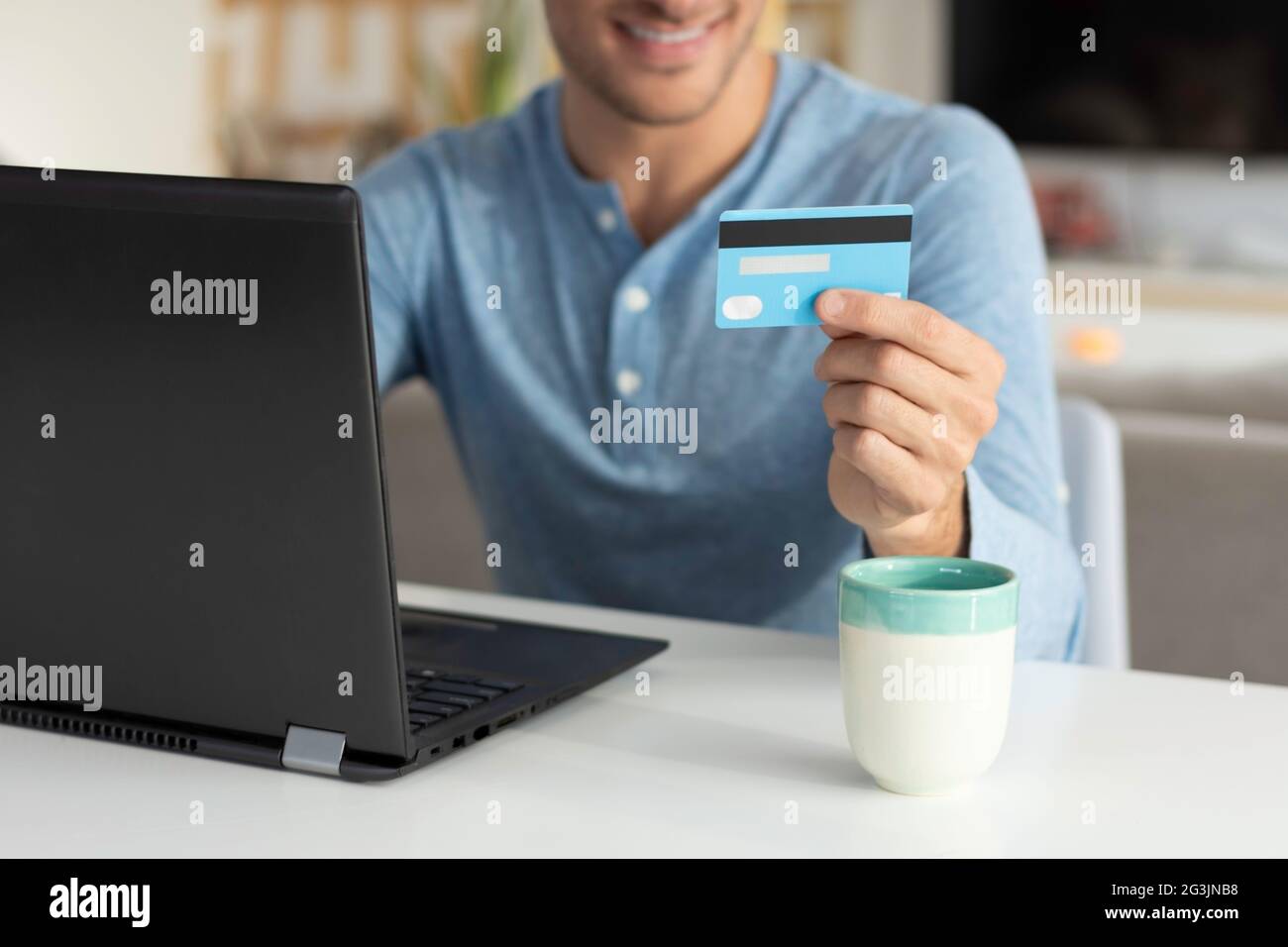 Junger Mann, der zu Hause eine Kreditkarte hält und Einkäufe tätigt Stockfoto