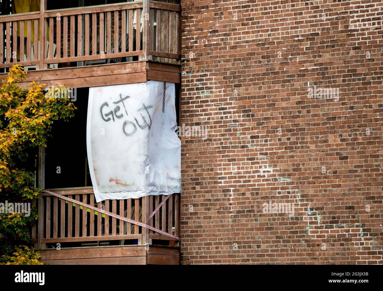 Ein Laken hing auf dem Deck eines gemauerten Wohnhauses. Auf dem Blatt stehen die Worte „Get out“. Rechts ist Platz für Text. Stockfoto