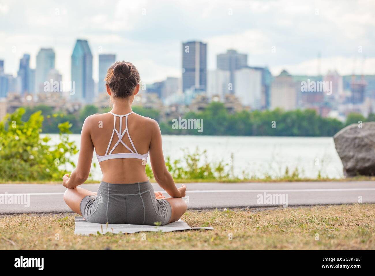 Zen-Yoga-Kurs draußen im Stadtpark Frau Wellness meditiert in Lotus Pose im Freien auf Matte und Gras. Mädchen von hinten sitzend Stockfoto