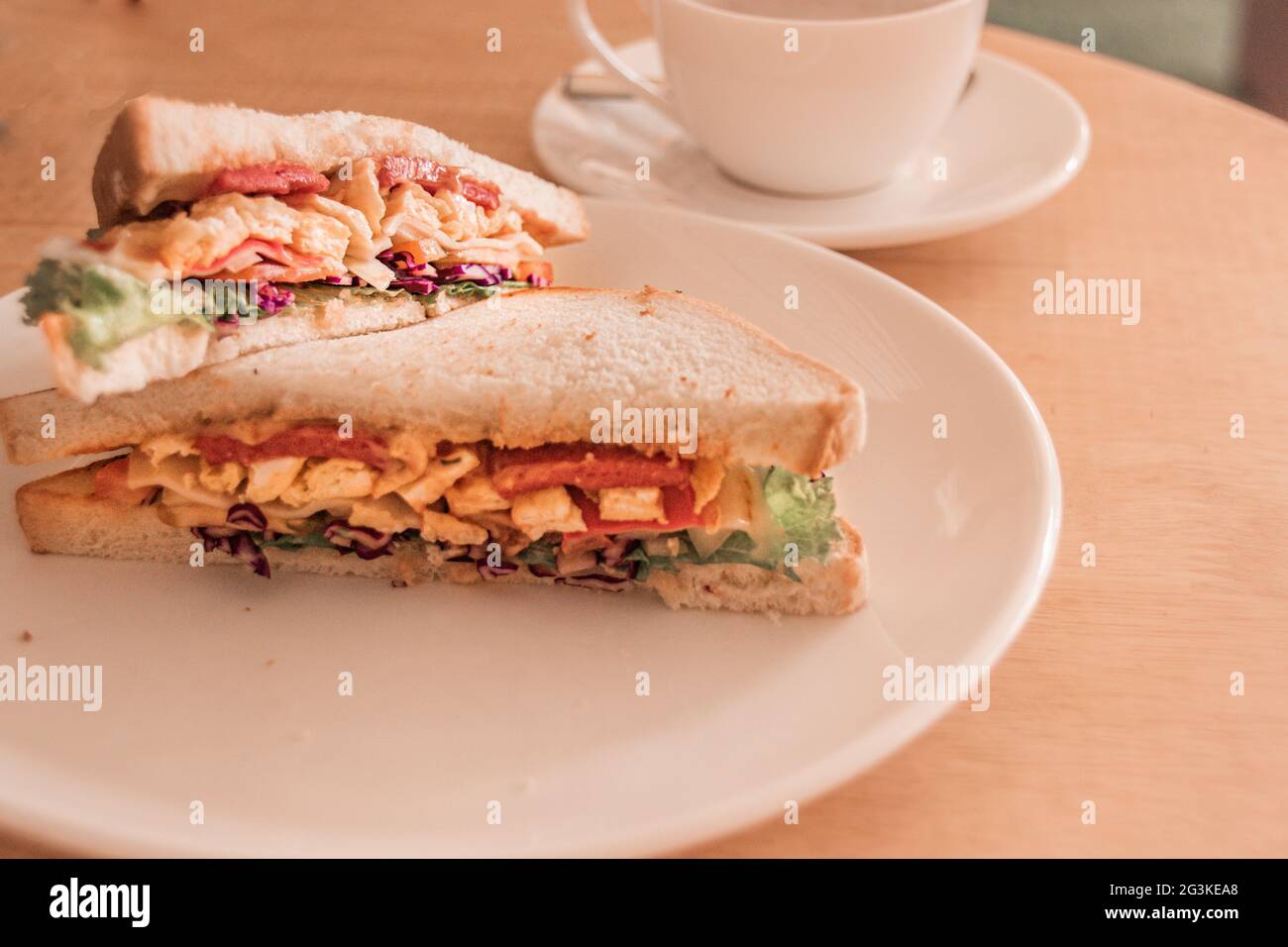 Shallow-Focus-Aufnahme eines leckeren Sandwiches auf einem weißen Teller mit einer Teetasse daneben Stockfoto