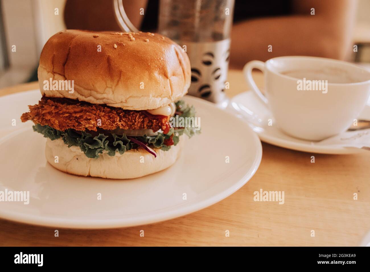 Shallow-Focus-Aufnahme eines leckeren Burgers auf einem weißen Teller mit einer Teetasse daneben Stockfoto