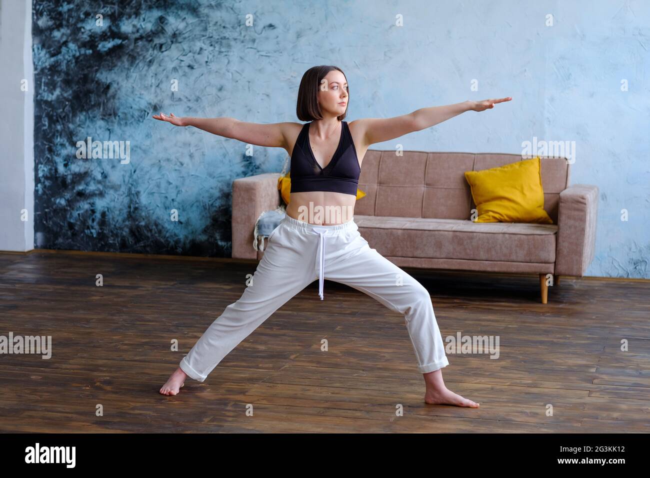 Frau in ihrem Wohnzimmer in Krieger-Yoga-Pose. Stockfoto