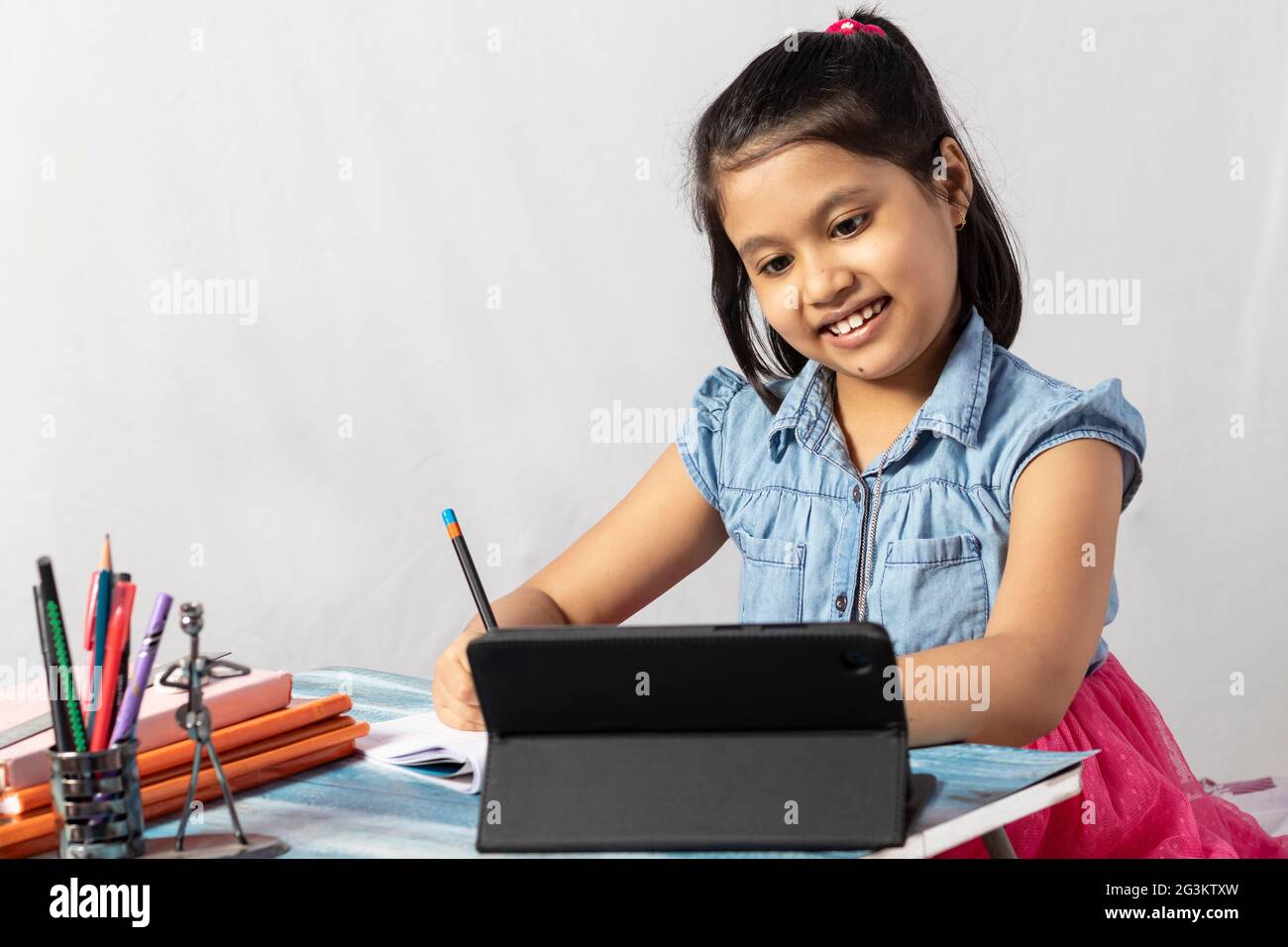 Ein hübsches indisches Mädchen, das am Online-Kurs mit Tablet auf weißem Hintergrund teilnimmt Stockfoto