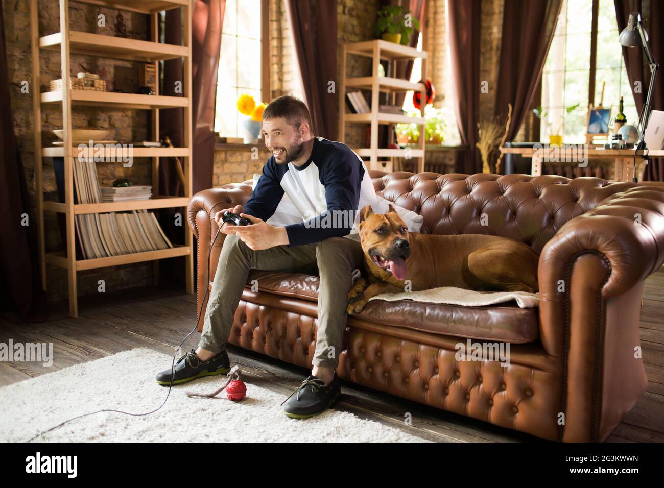 Hübscher Kerl sitzt auf einem Sofa mit seinem Hund, spielen video game. Stockfoto