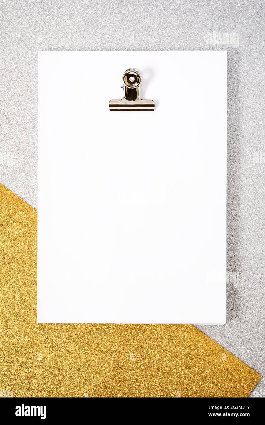Weißes Papierblattbündel und Büroklammer auf Gold- und silberfarbenem texturiertem Hintergrund. Das Foto hat einen Kopierbereich und wird aus der Sicht des Überkopfs aufgenommen Stockfoto