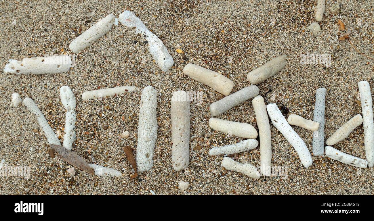 Sand mit weißen Korallenstücken am Strand von Curacao. Es sieht aus wie ein unbekanntes Skript. Es ist Papiamentu. Pabien = Happy Birthday Stockfoto
