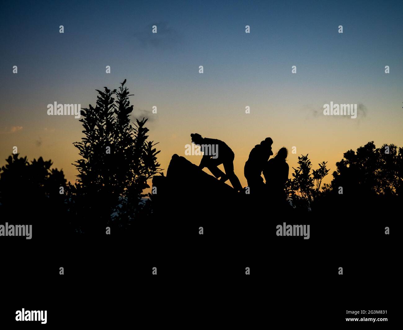 Silhouetten von begeisterten Wanderern sitzen auf einem Felsen, um den Sonnenaufgang zu beobachten Stockfoto