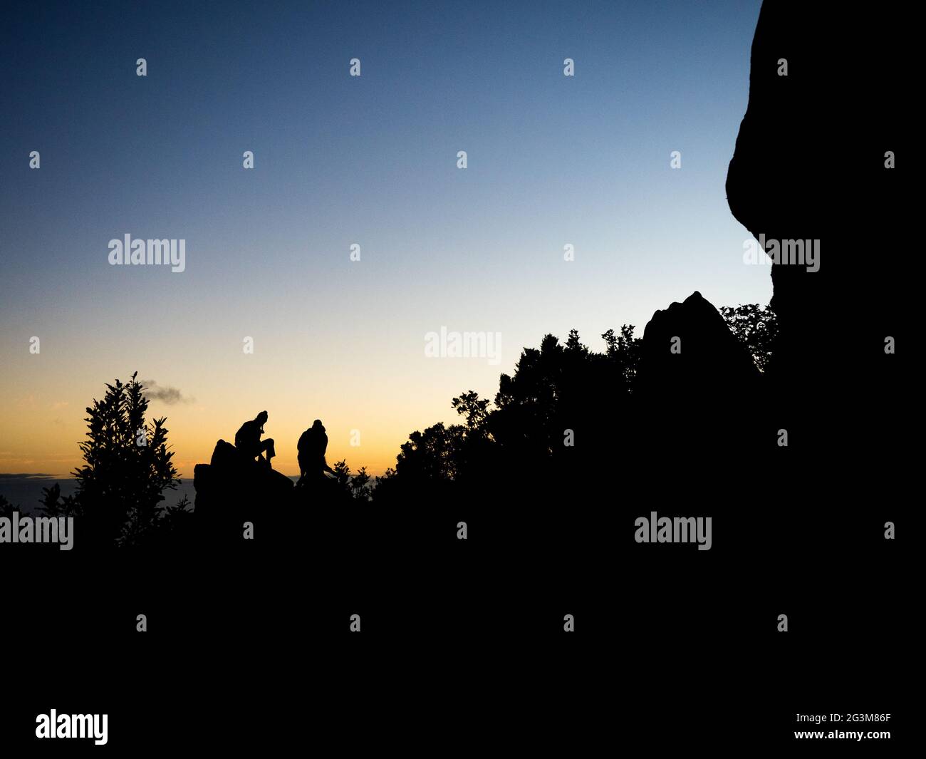 Silhouetten von begeisterten Wanderern sitzen auf einem Felsen, um den Sonnenaufgang zu beobachten Stockfoto