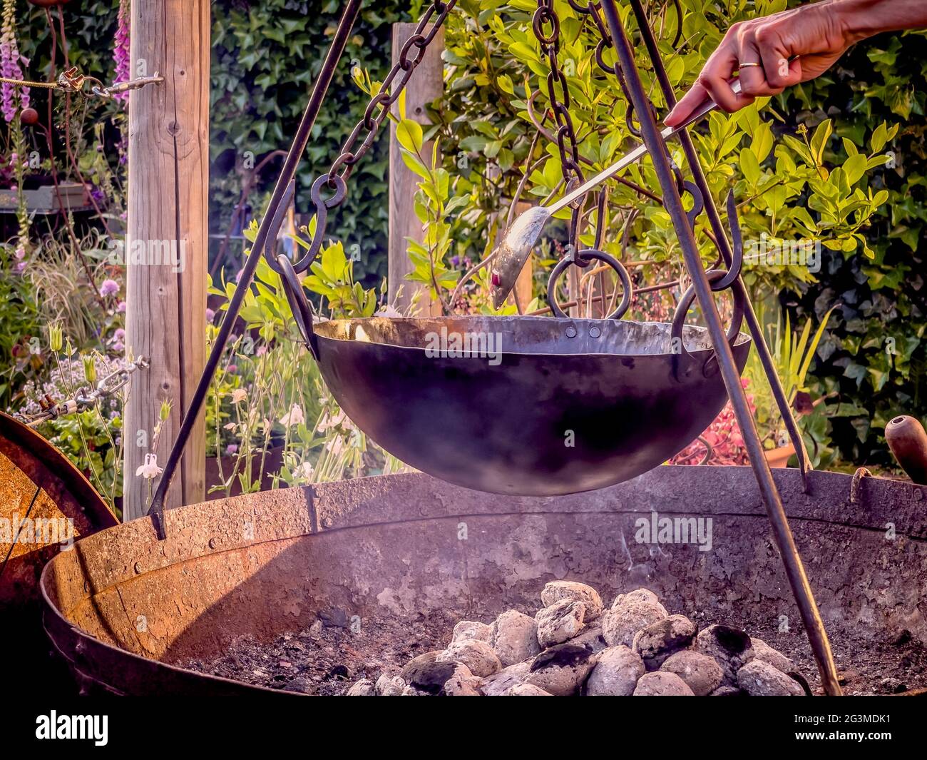 Kochen im Freien mit Holzkohle in Feuerbecken mit Stativ und Topf, der an Ketten hängt Stockfoto