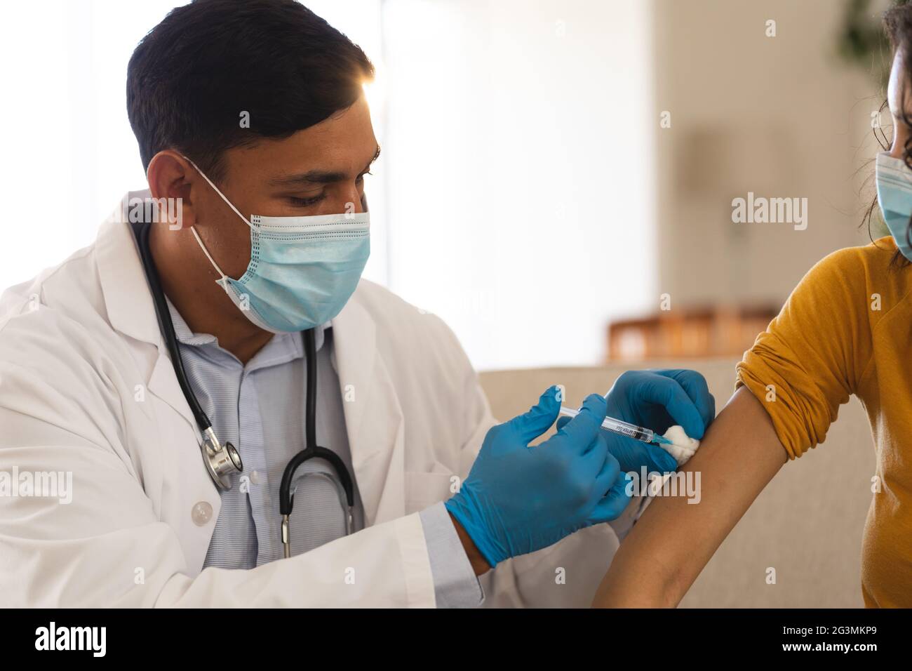 Hispanischer Arzt, der weiblichen Patienten zu Hause eine Covid-Impfung mit Gesichtsmasken verabreicht Stockfoto