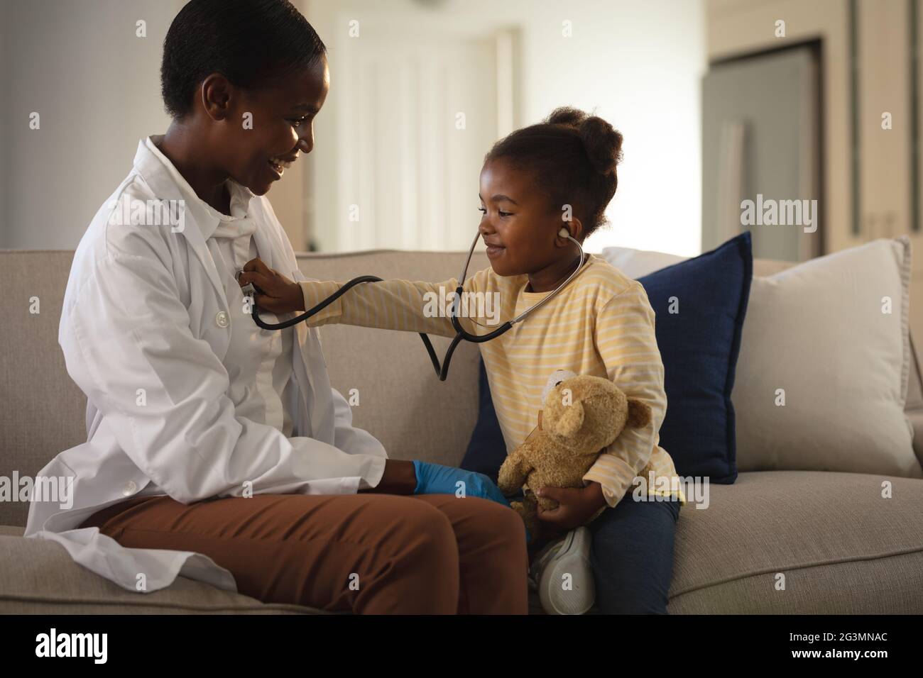 Lächelnde afroamerikanische Ärztin, die zu Hause eine Patientin besucht und mit dem Stethoskop spielt Stockfoto