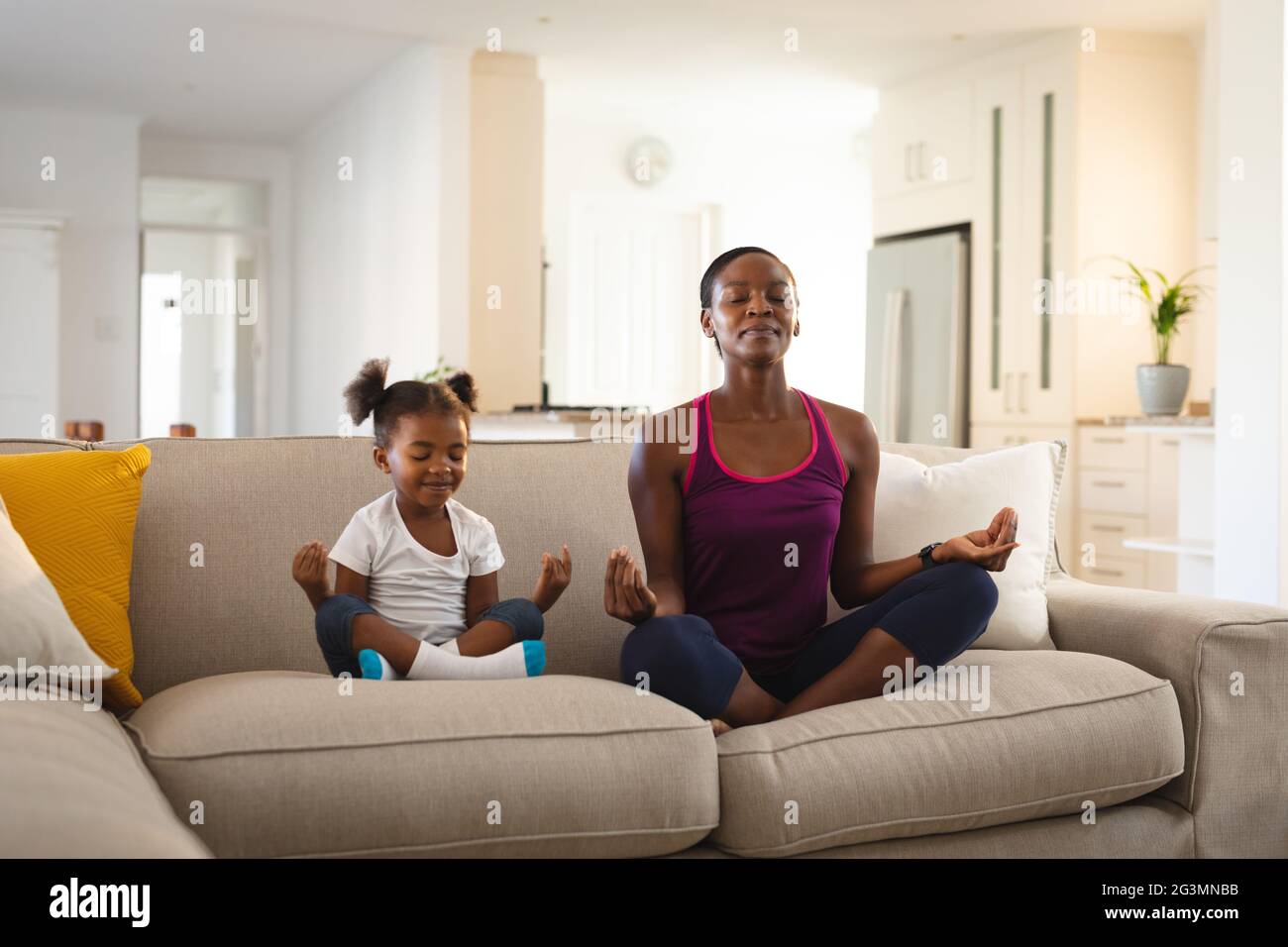 Glückliche afroamerikanische Mutter und Tochter praktizieren Yoga und meditieren auf der Couch im Wohnzimmer Stockfoto