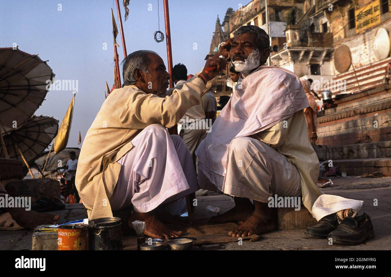 '13.04.2014, Varanasi, Uttar Pradesh, Indien - EIN Straßenbarbier rasiert einen Kunden an einem Ghat am Ufer des heiligen Ganges am Morgen. 0SL100324D00 Stockfoto