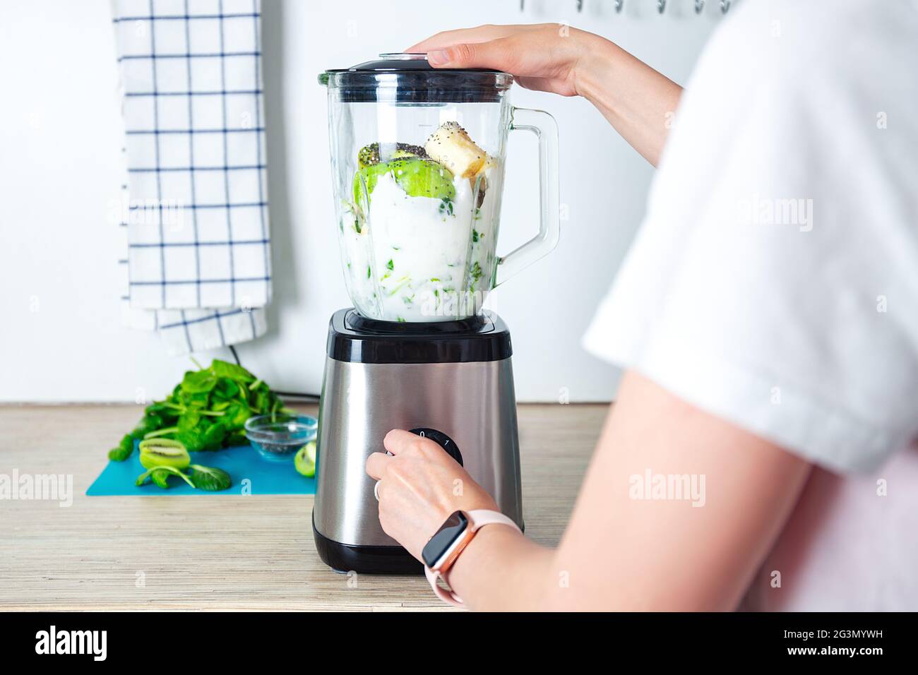 Junge Frau bereitet gesunde Lebensmittel in der hellen Küche zu. Green Healthy Food Konzept. Vegetarischer grüner Cocktail aus Spinat, Brokkoli und Kokosmilch. Stockfoto