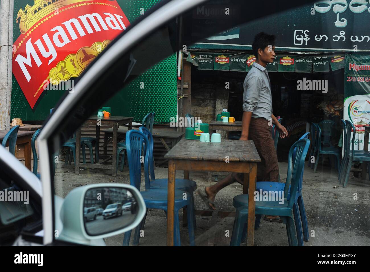 '10.02.2014, Yangon , , Myanmar - EIN Mann in einem traditionellen Umhang geht an leeren Tischen in einem Restaurant am Straßenrand im Zentrum des ersteren vorbei Stockfoto