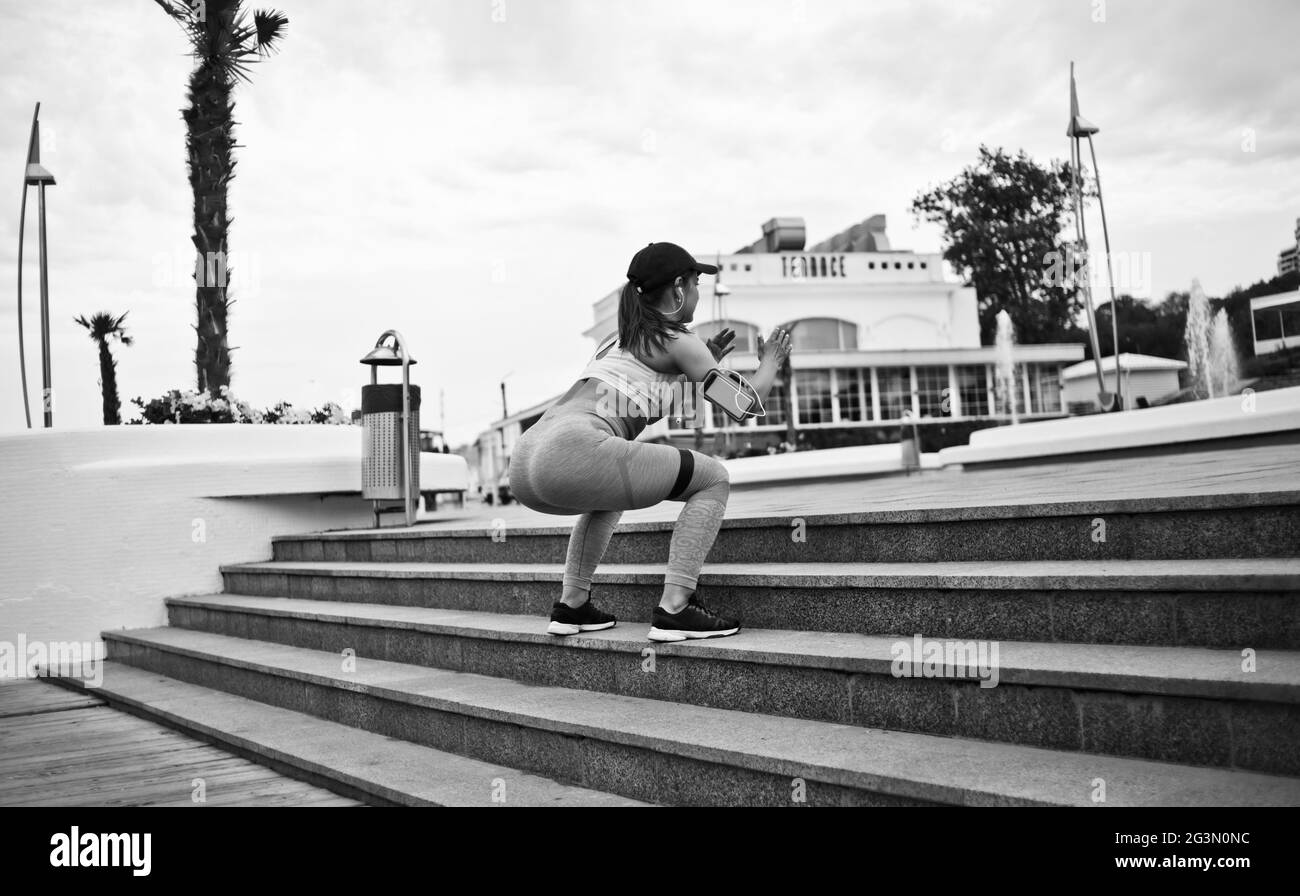 Fit Frau in Sportswear Sprünge mit Fitness-Gummi Expander auf der Treppe im Freien. Funktionales Training auf der Straße. Rückansicht Stockfoto