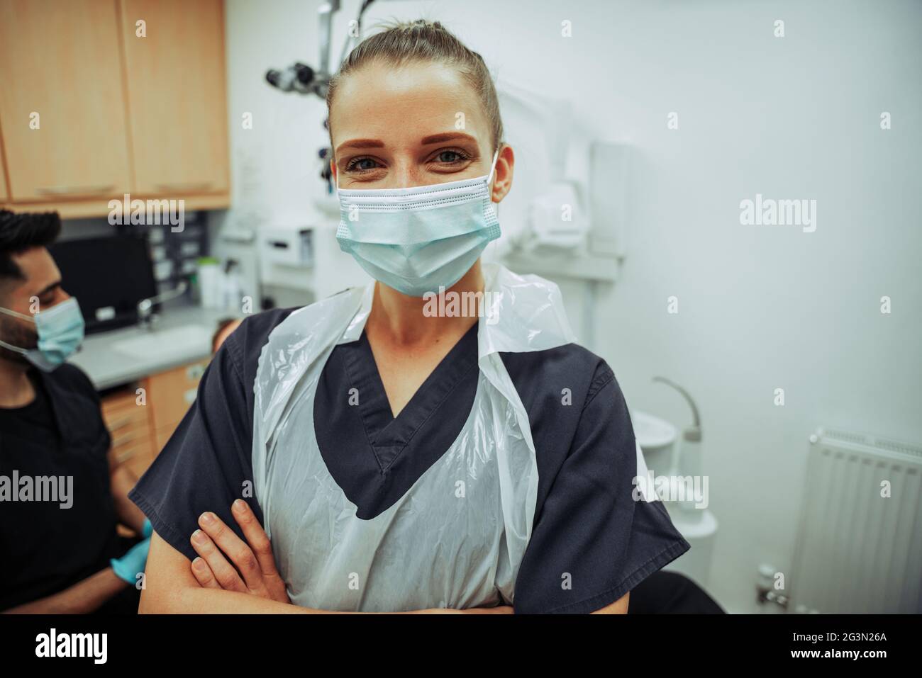 Kaukasische Krankenschwester, die lächelt und eine OP-Maske trägt, während sie mit einem männlichen Kollegen im Zimmer des Arztes steht Stockfoto