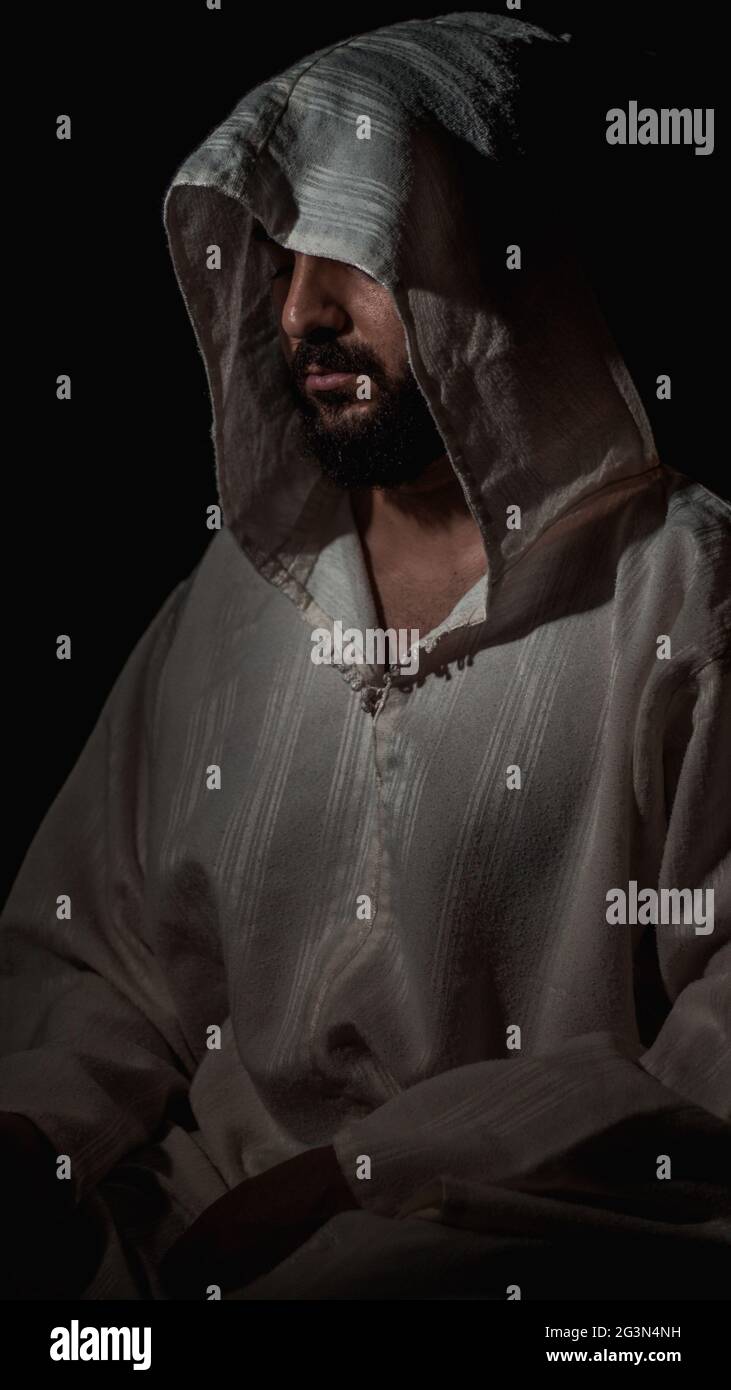 Ein afrikanischer muslimischer Mann mit einem Bart, der an einem dunklen Ort betet, trägt eine traditionelle weiße marokkanische Djellaba Stockfoto