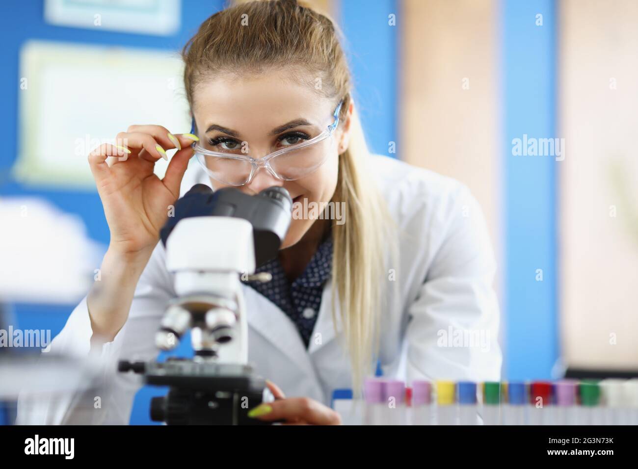 Chemikerin in einer Sicherheitsbrille, die im Labor durch das Mikroskop schaut Stockfoto