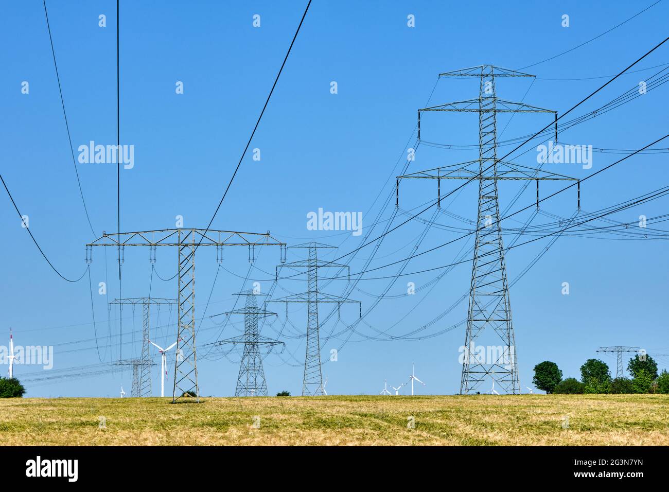 Strommasten und Stromleitungen mit Windturbinen im Hintergrund Stockfoto