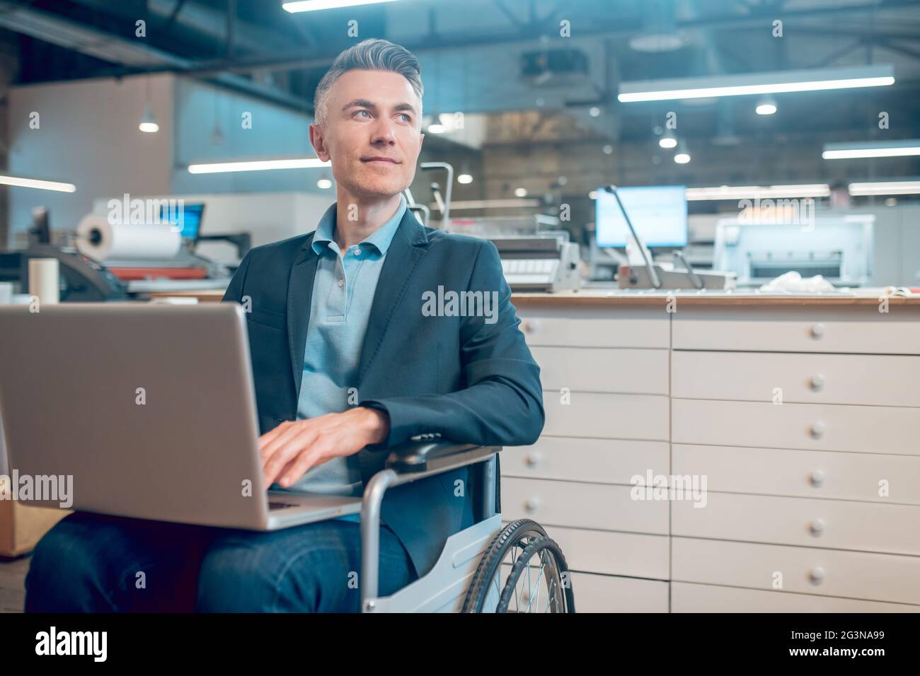 Mann mit Laptop im Rollstuhl, der zur Seite schaut Stockfoto