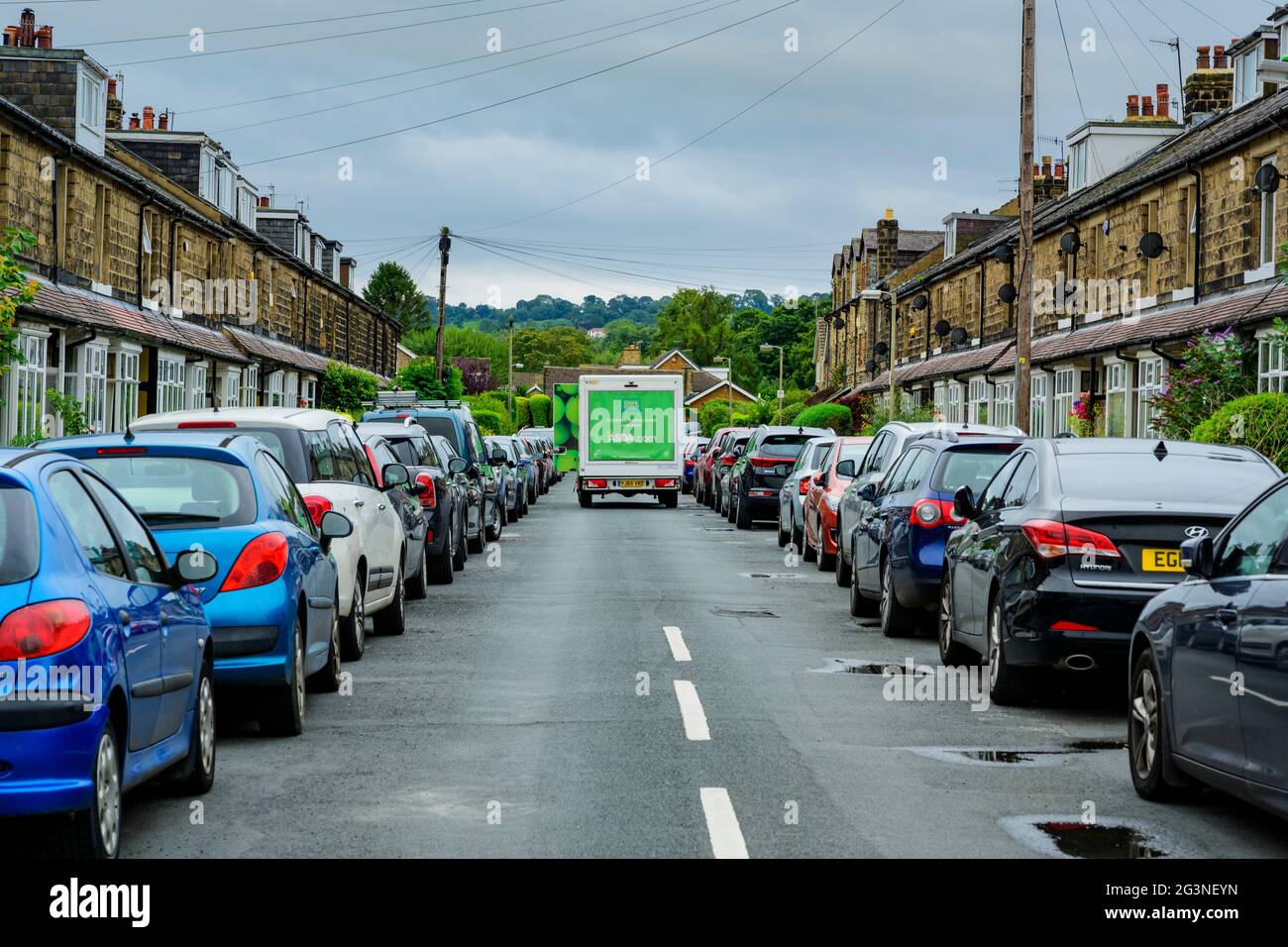 Asda Lieferwagen parkte auf der Straße (Route blockiert) zwischen den Reihen geparkter Fahrzeuge außerhalb von Steinterrassenhäusern - Burley in Wharfedale, Yorkshire, Großbritannien. Stockfoto