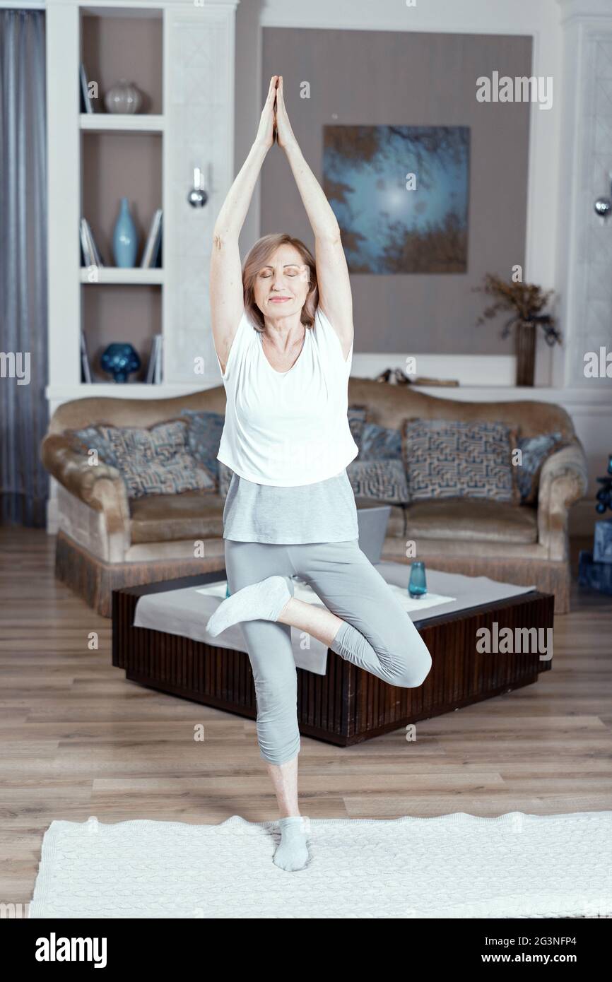 Eine 50 Jahre alte Frau übt Yoga zu Hause im Wohnzimmer. Stockfoto