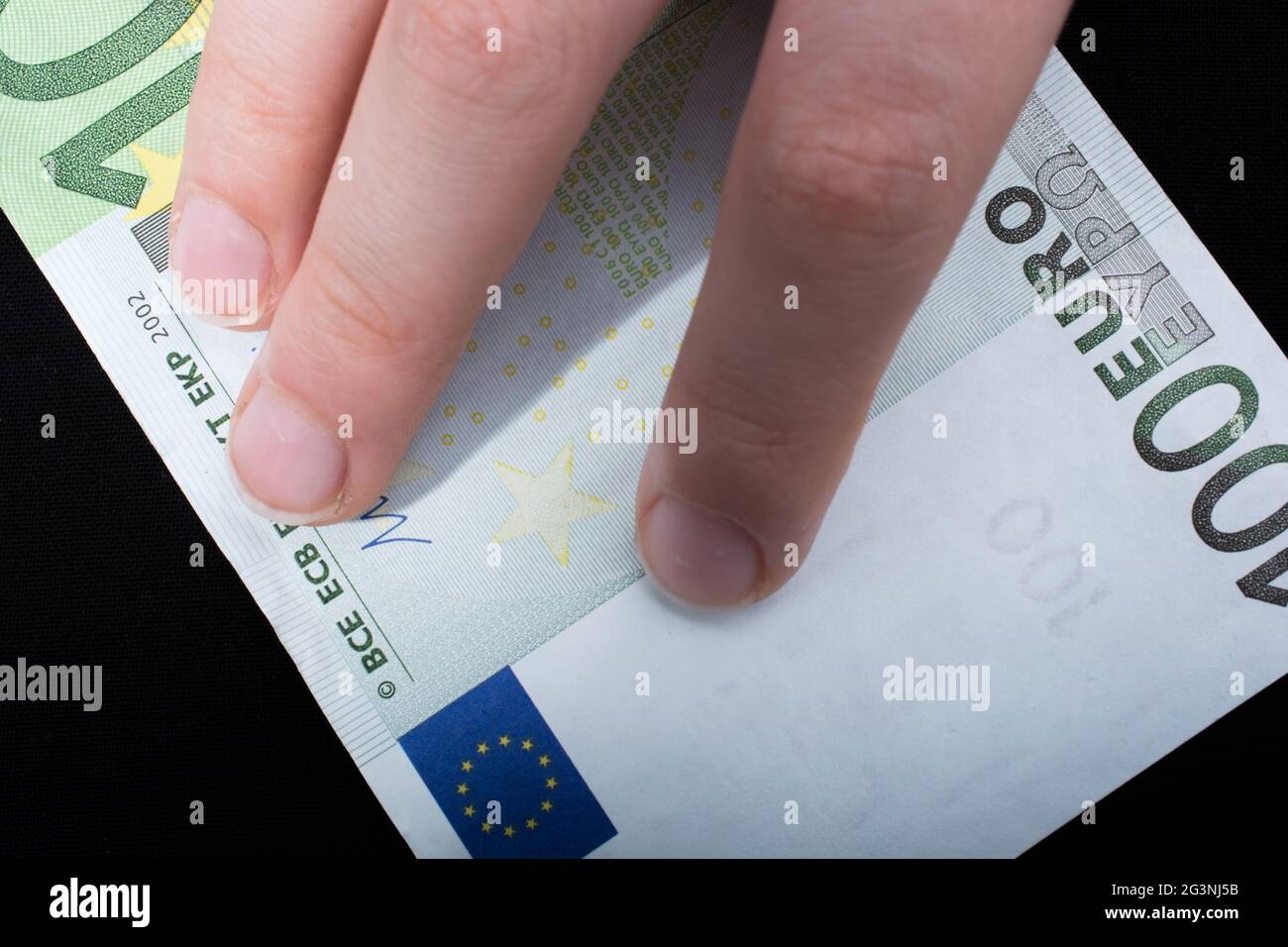Hand mit 100-Euro-Banknote auf schwarzem Hintergrund Stockfoto