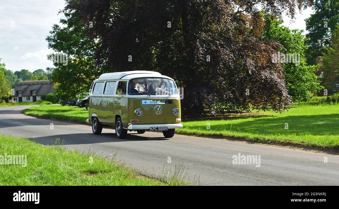 Klassischer Volkswagen Camper Van, der durch Dorfhaus und Bäume im Hintergrund fährt. Stockfoto