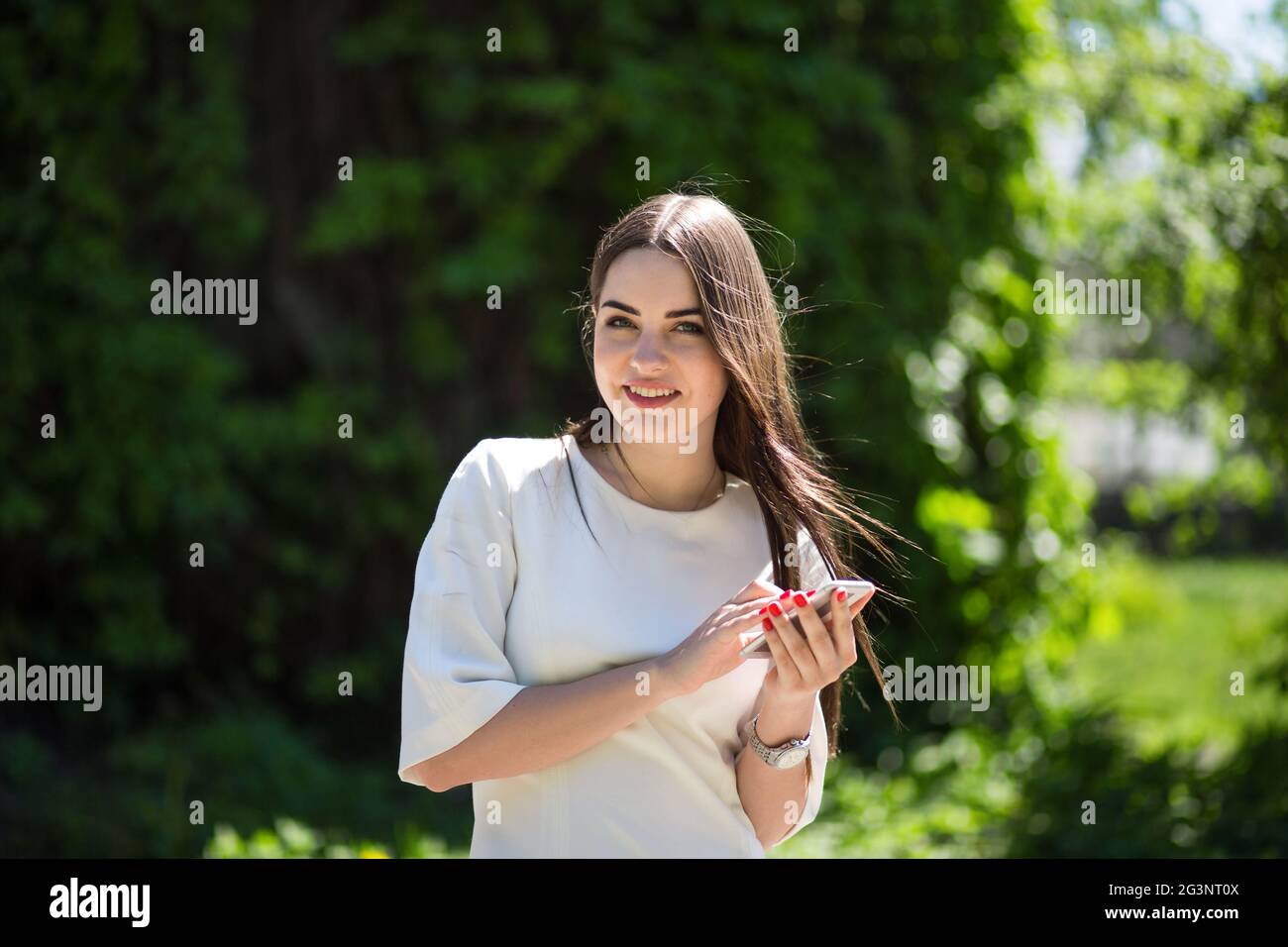 Lächelnde Junge brünette Frau hält Ihr Telefon im Park. Stockfoto