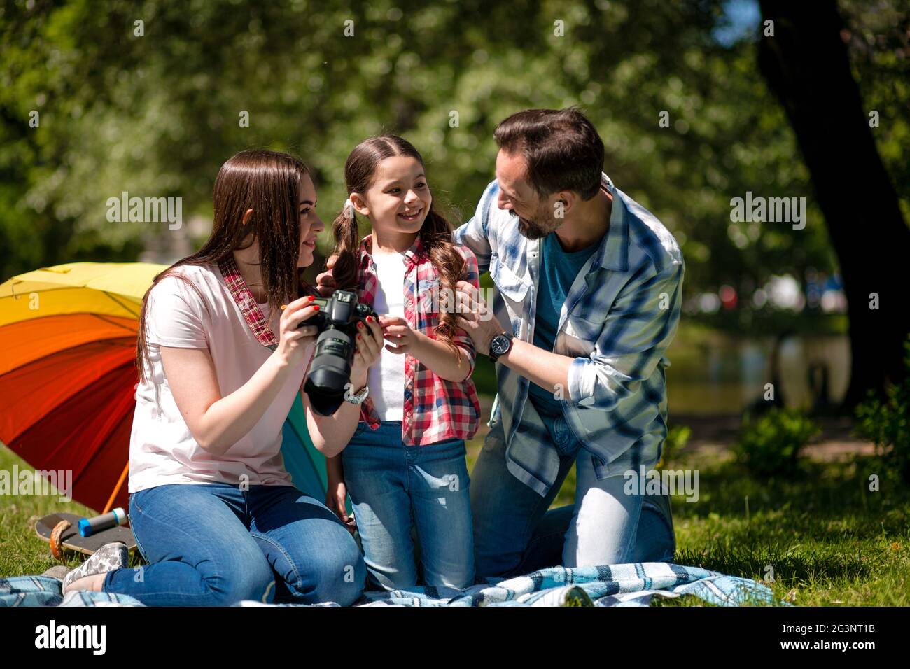Junge Frau zeigt Fotos an ihren Mann und ihre Tochter beim Sitzen auf Decke im Park. Stockfoto