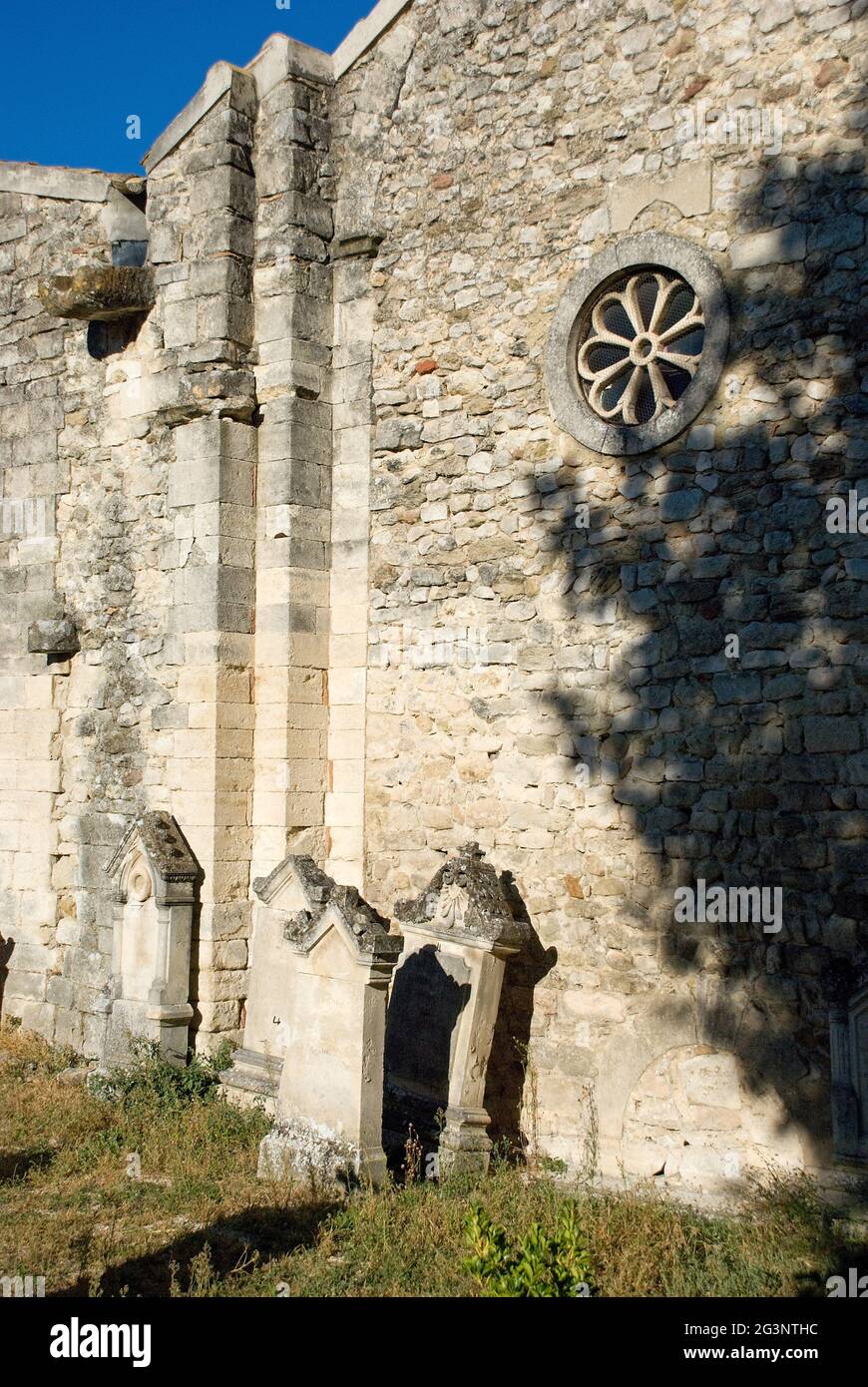Steinkreuz und Grabsteine vor der Kirchenmauer Stockfoto