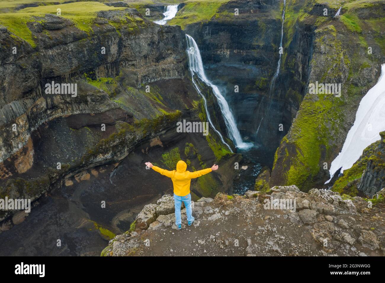 Luftaufnahme eines Mannes in gelber Jacke Heben Sie die Hände hoch und genießen Sie das isländische Hochlandtal und den Wasserfall. Island Stockfoto