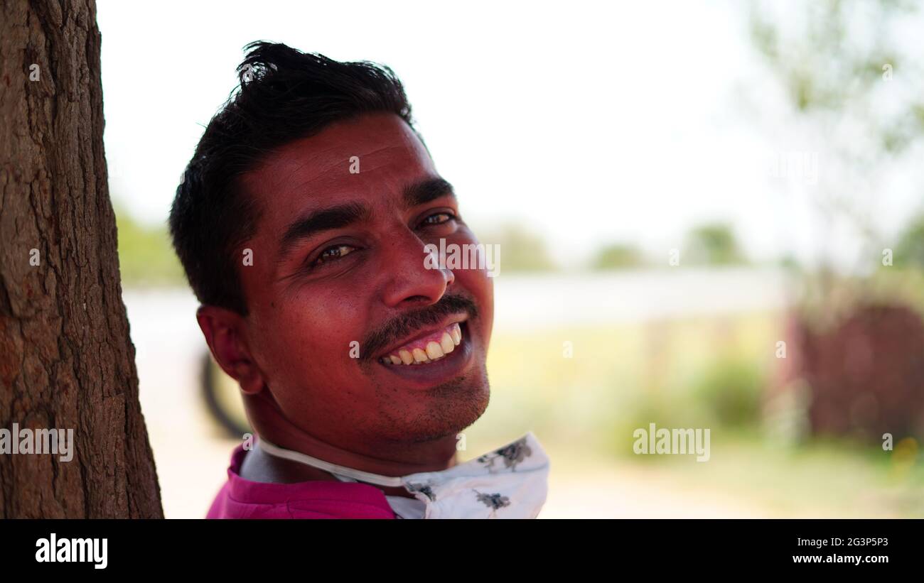 Porträt eines lächelnden indischen jungen Mannes mit hartem hellen Hintergrund. Glücklicher asiatischer Mann, der die Kamera im Freien anschaut. Stockfoto