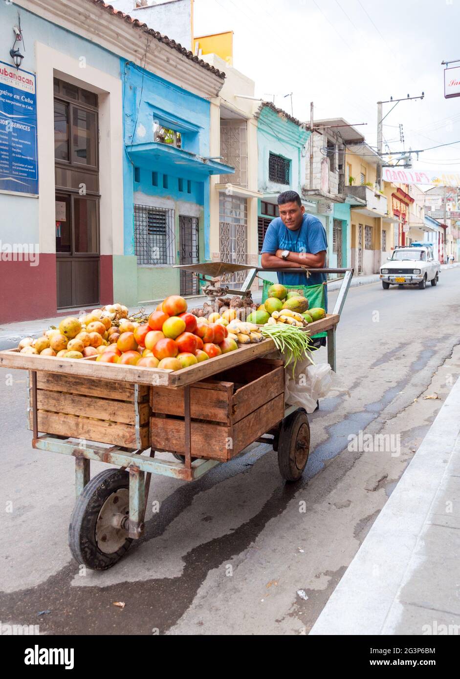 Kuba beginnende Marktgesellschaft: Straßenfrucht-Verkäufer trägt Waren auf einem Wagen auf der Straße kubanische Stadt mit dem alten Auto im Hintergrund Stockfoto