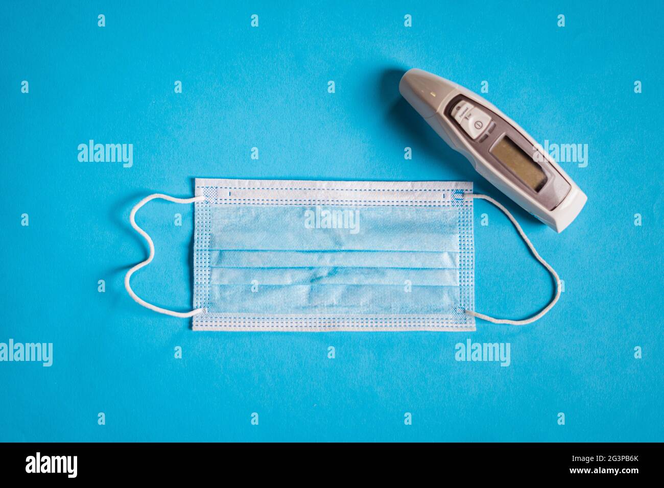 Medizinische Gesichtsmaske und Thermometer auf blauem Hintergrund. Corona-Virenschutz. Stockfoto
