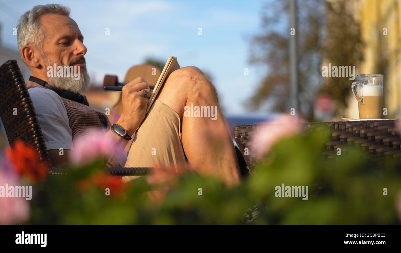 Der erfolgreiche Schriftsteller notiert begeistert an einem sonnigen Morgen in einem Café Stockfoto