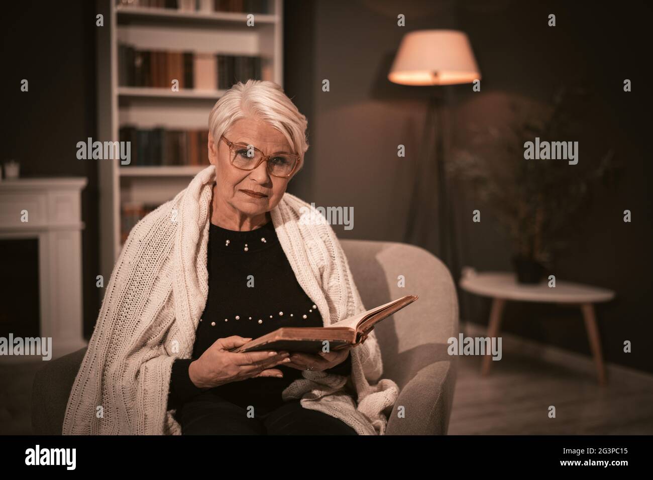 Ältere Frau liest auf einem Stuhl sitzend das alte Buch. Stockfoto